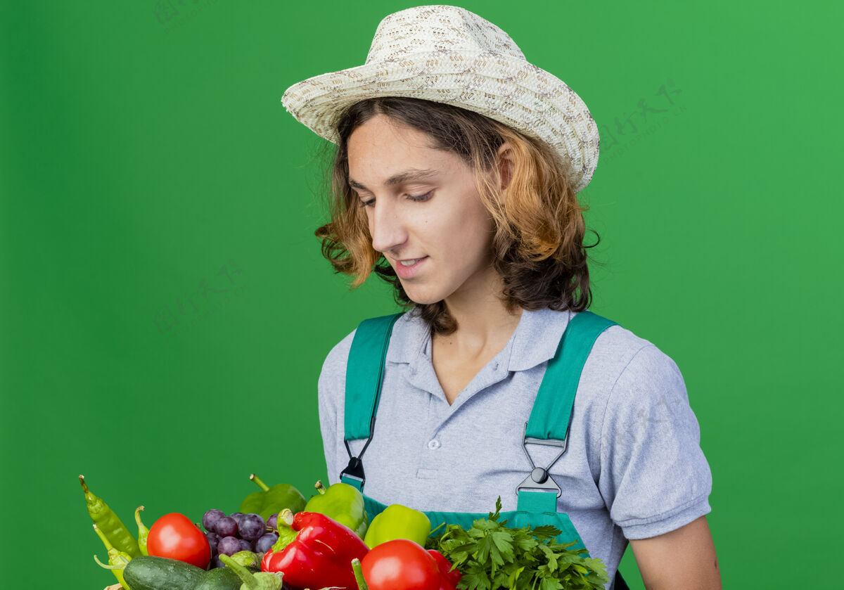 箱子年轻的园丁穿着连体衣戴着帽子拿着装满新鲜蔬菜的箱子新鲜男人年轻
