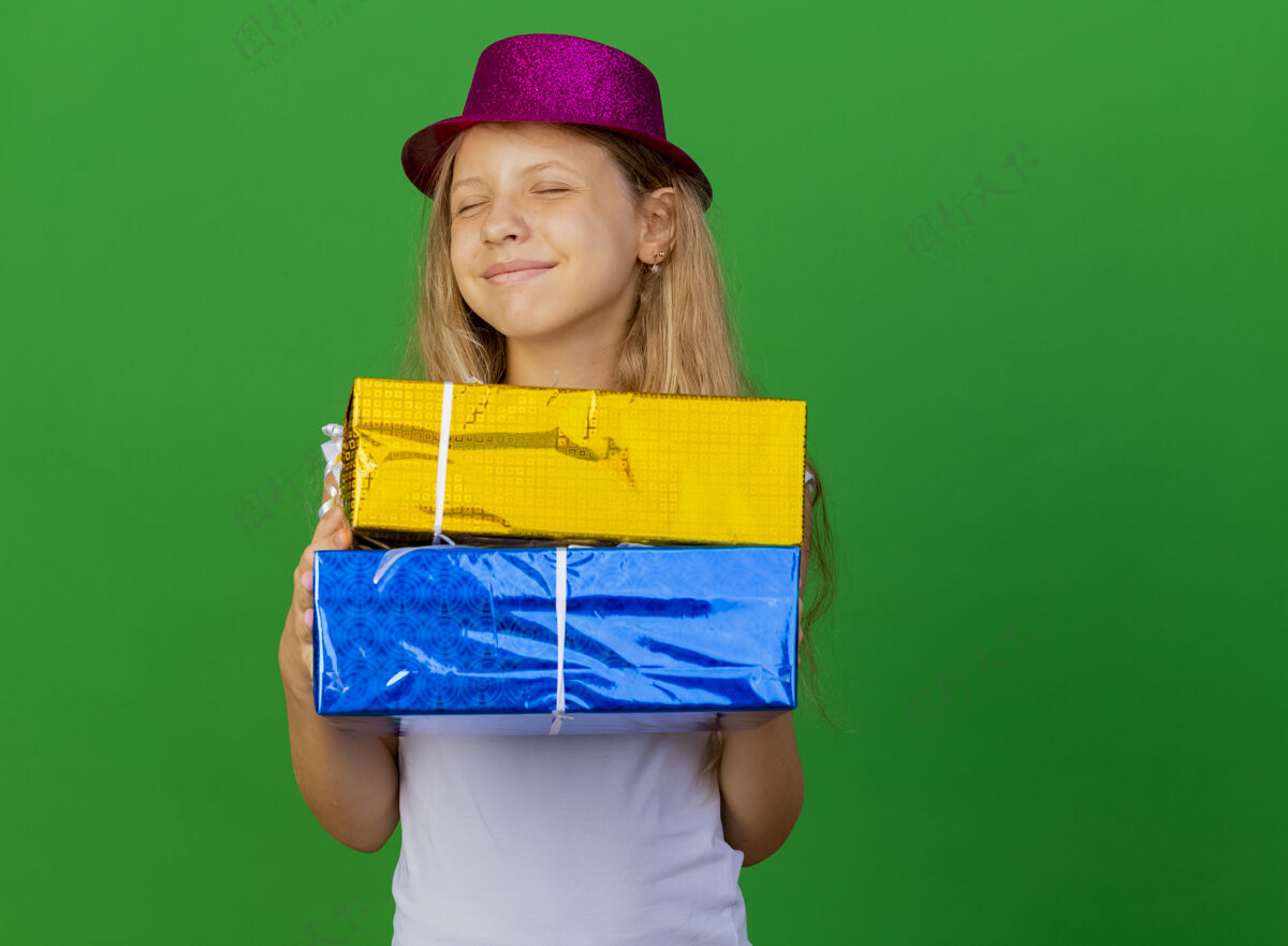 抱着戴着节日帽子拿着礼品盒的漂亮小女孩小快乐盒子
