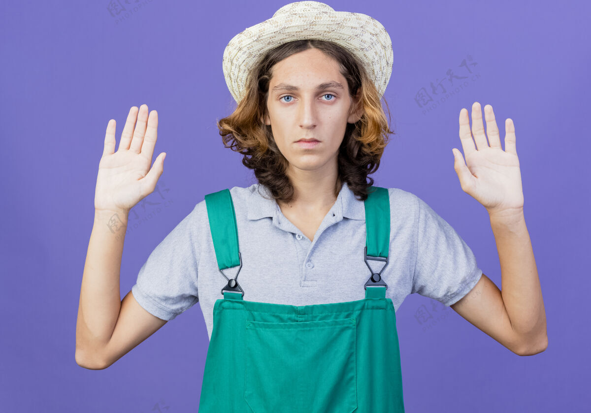 连身衣年轻的园丁 穿着连体衣 戴着帽子 一脸严肃地抬起手掌穿严肃年轻人