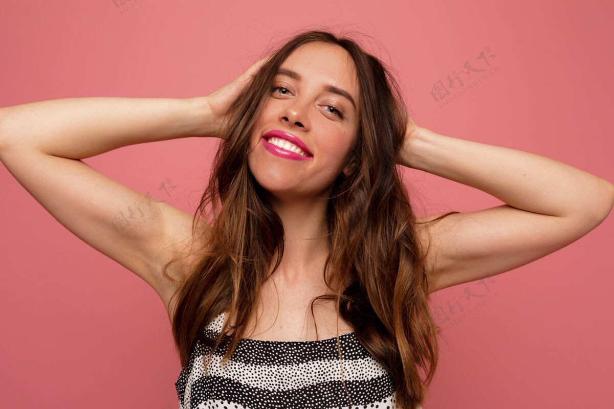 微笑快乐的难以置信的女人 波浪形的头发 在粉红色的墙上摆出快乐的微笑牙齿嘴唇嘴巴