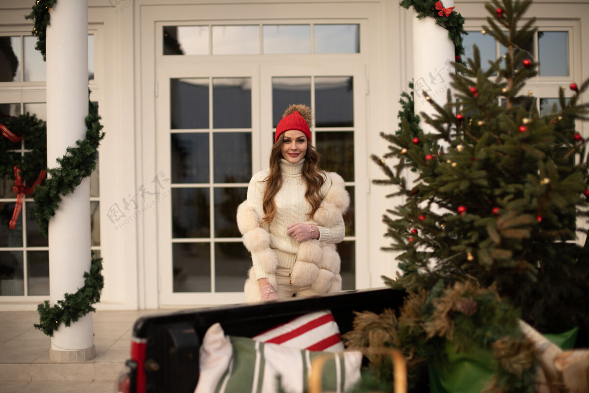 云杉微笑的年轻女子穿着冬暖的衣服走在家附近舒适女性圣诞树