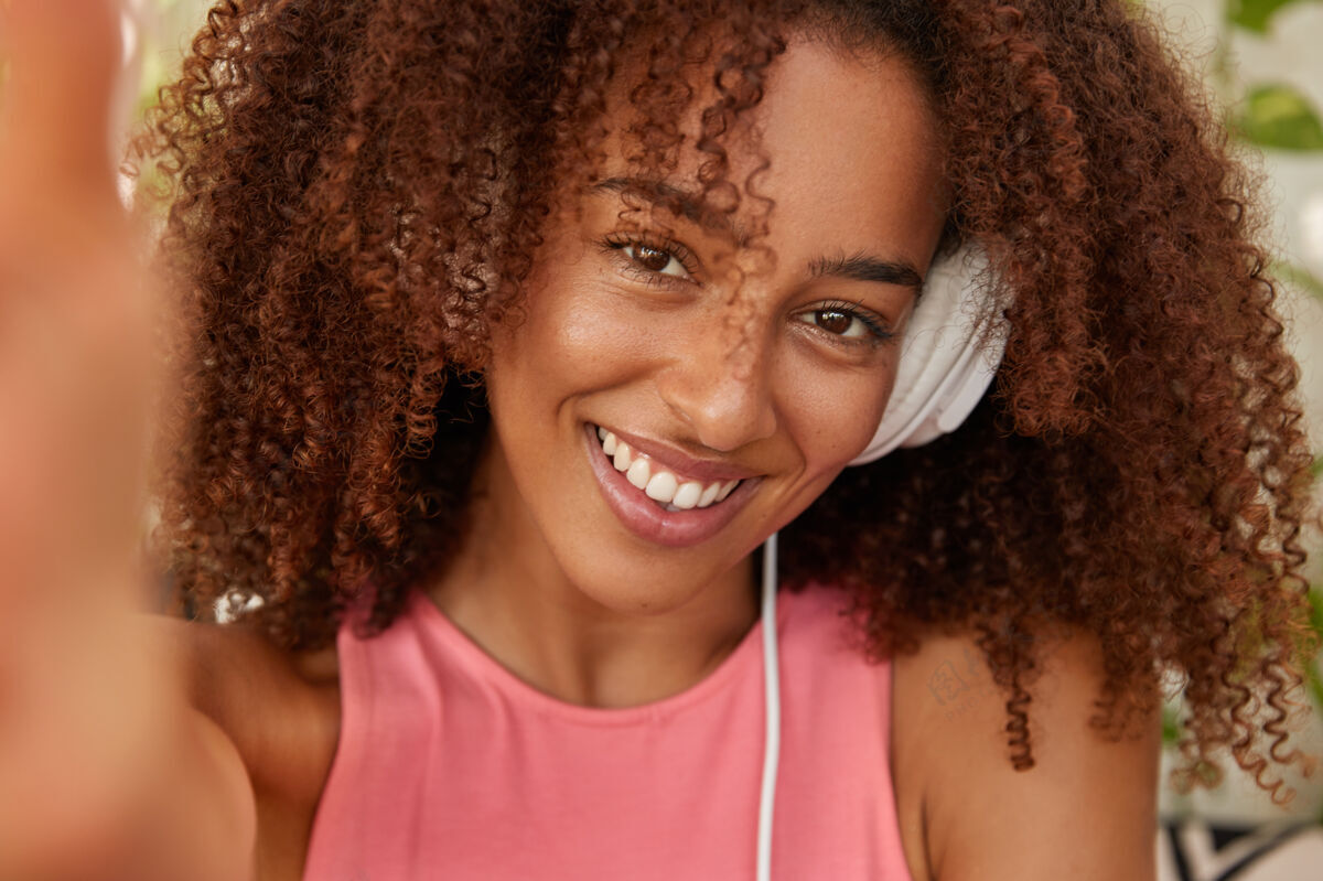 姿势积极的黑人妇女用耳机收听最喜爱的播放列表暗哑女士时髦