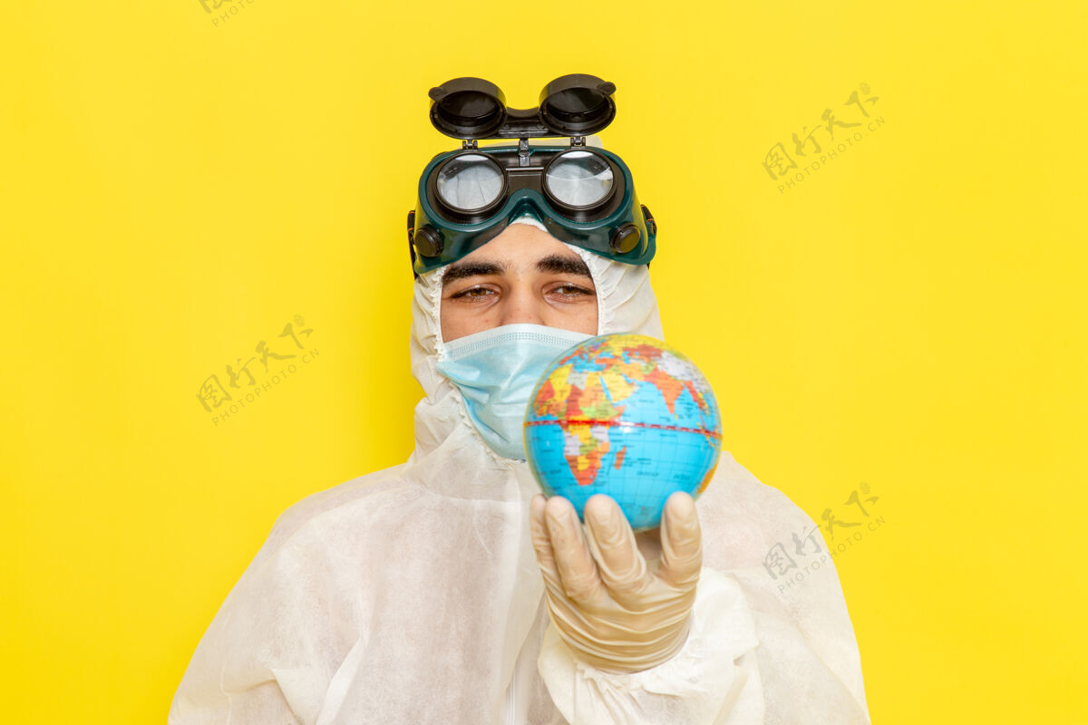 西装正面近距离看黄色办公桌上手持小圆地球仪的身着特殊套装的男科学工作者科学服装地球仪