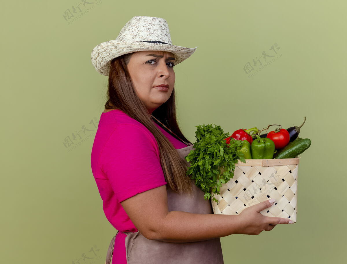 板条箱围裙戴帽子的中年园丁妇女拿着装满蔬菜的板条箱光帽子脸