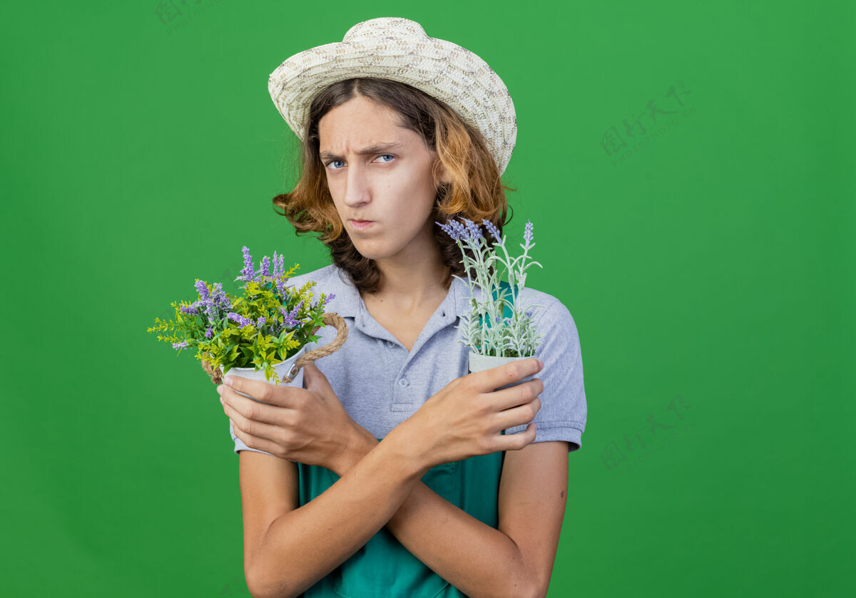 穿年轻的园丁 穿着连体衣 戴着帽子 手里拿着盆栽植物男人皱眉帽子