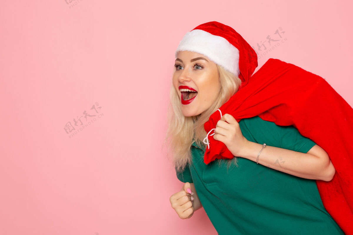 圣诞节正面图年轻女性拎着红包带着礼物上了粉红色的墙壁模型假日圣诞老人新年照片彩色圣诞老人风景圣诞老人颜色