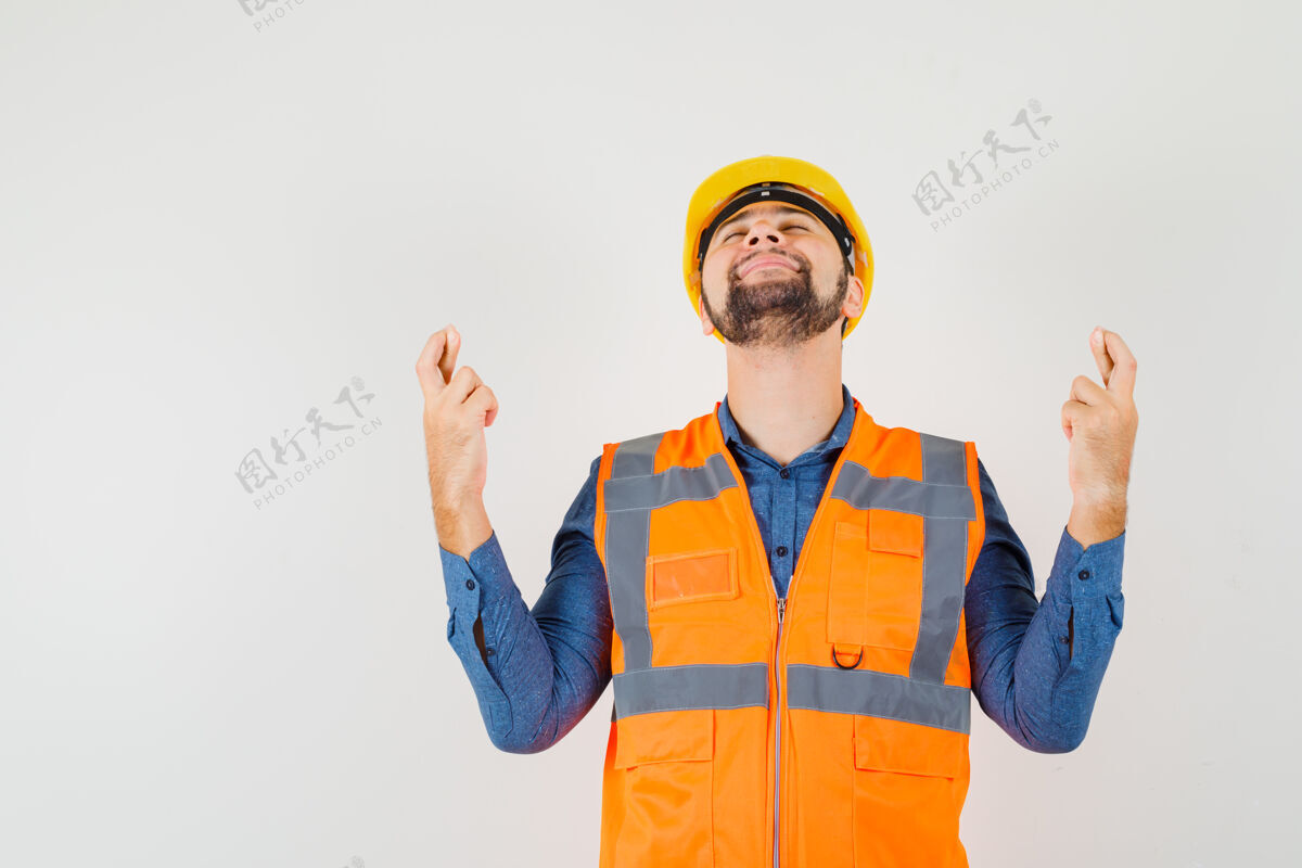 工作年轻的建筑工人在衬衫 背心 头盔上交叉着手指 看上去很平静前视图头盔背心制服