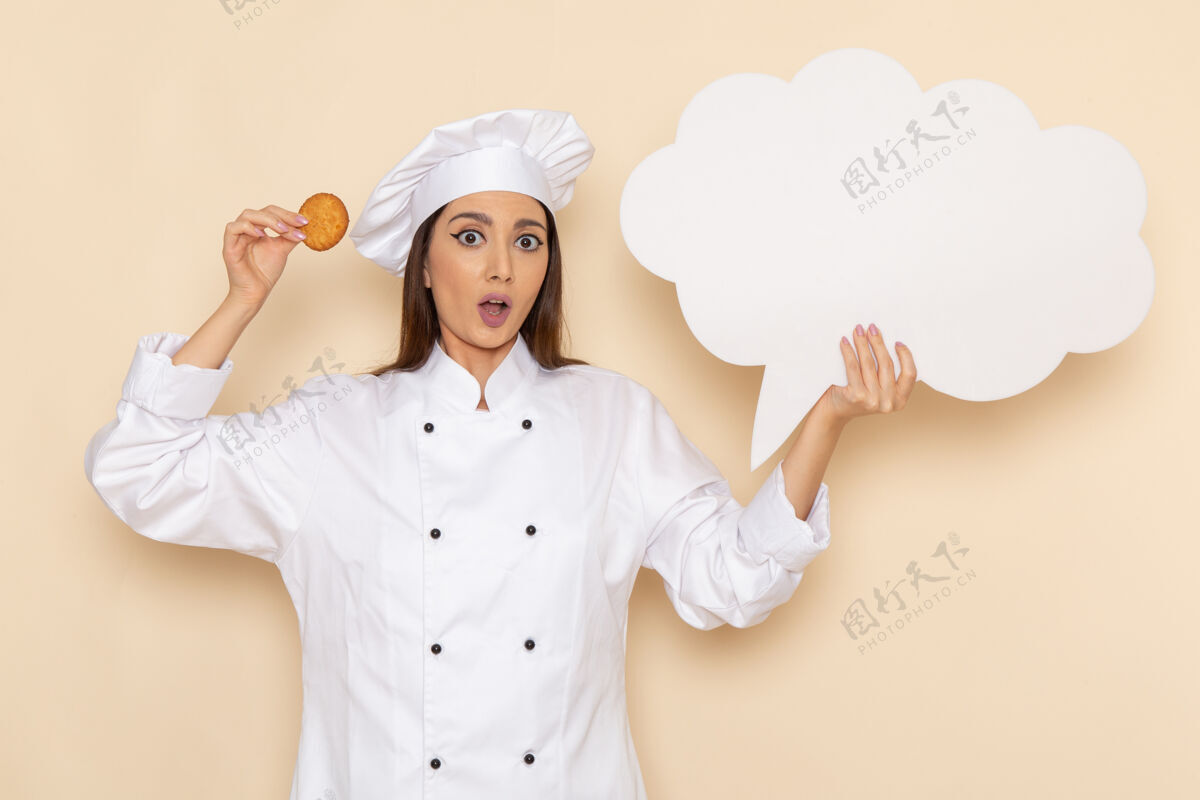 肖像身穿白色厨师服的年轻女厨师正拿着饼干站在浅白的墙上年轻前面脸