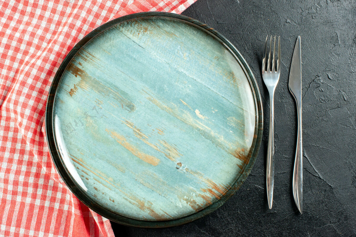 煎锅顶视图圆盘钢叉和餐刀红白格子桌布放在黑桌子上钢桌布金属