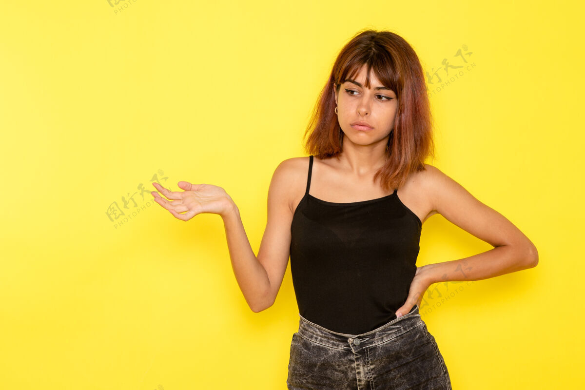 女性身穿黑色衬衫和灰色牛仔裤的年轻女性在黄色墙壁上摆姿势的前视图前面女孩姿势