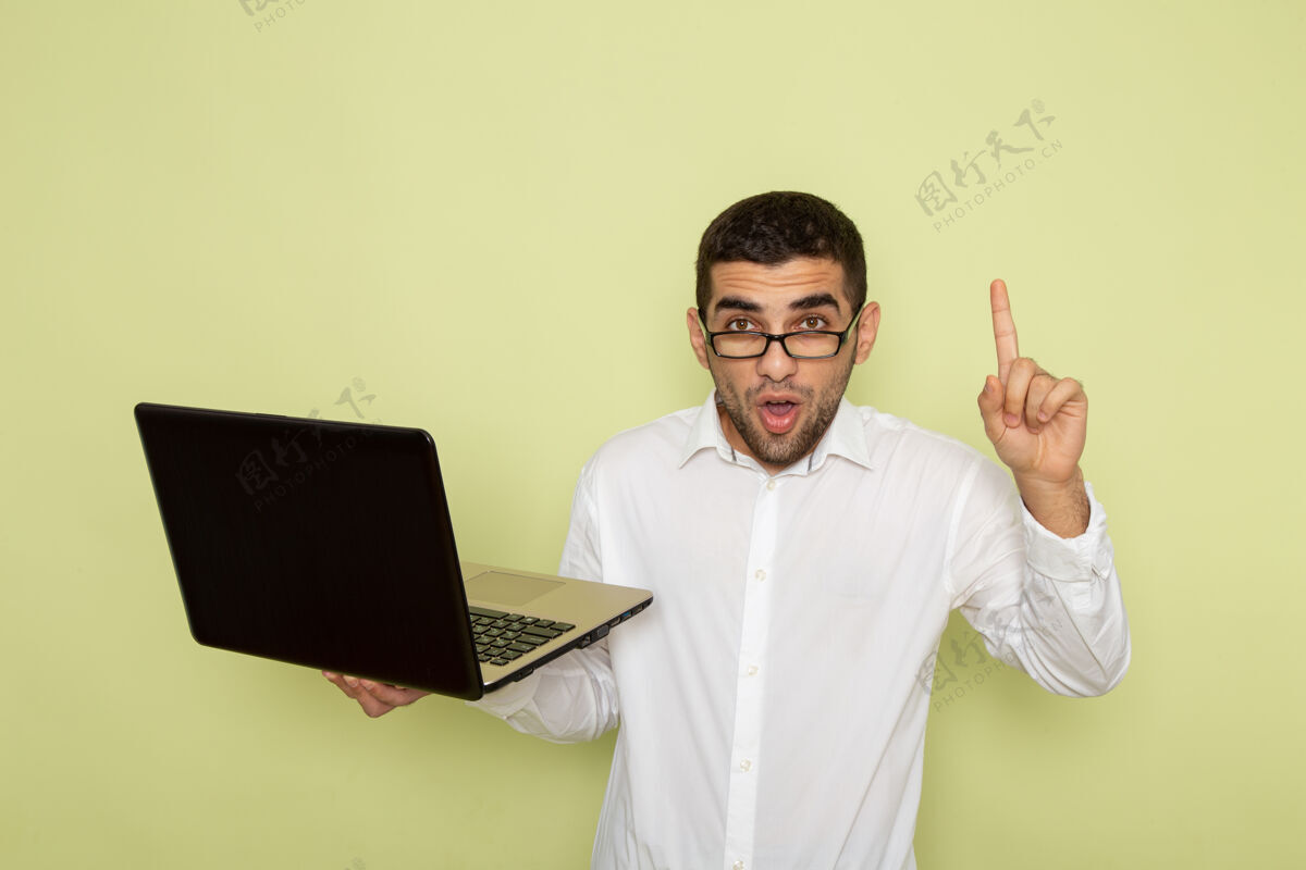 男性身穿白衬衫的男办公室工作人员手持和使用浅绿色墙上的笔记本电脑的正面视图衬衫办公室笔记本电脑