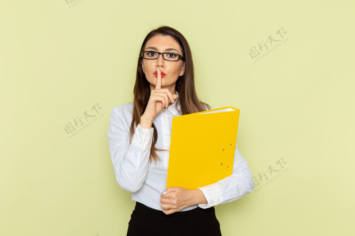 人身穿白衬衫和黑裙子的女上班族在绿色墙壁上举着黄色文件的正面视图快乐办公室业务