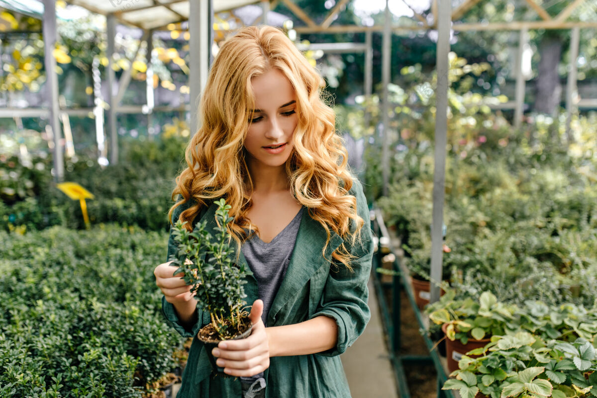金发年轻的植物爱好者走过植物园可爱的金发女孩饶有兴趣地看着植物享受可爱植物