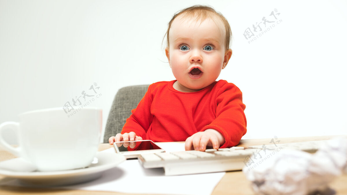 互联网小女婴坐在白色工作室里 用现代电脑或笔记本电脑的键盘老板孩子电话