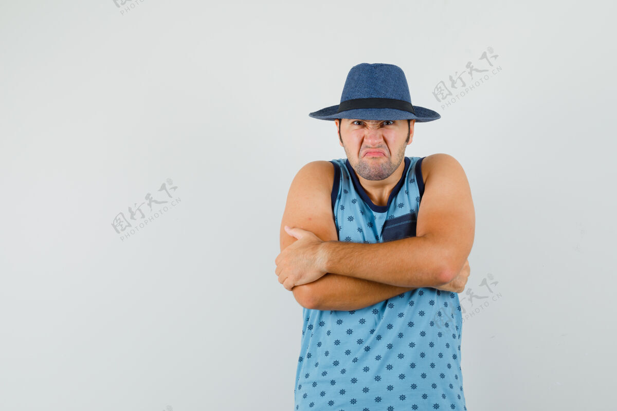 男性一个穿着蓝色单品的年轻人 戴着一顶帽子 双臂紧紧交叉着站着 满脸怨恨胡茬单身怨恨