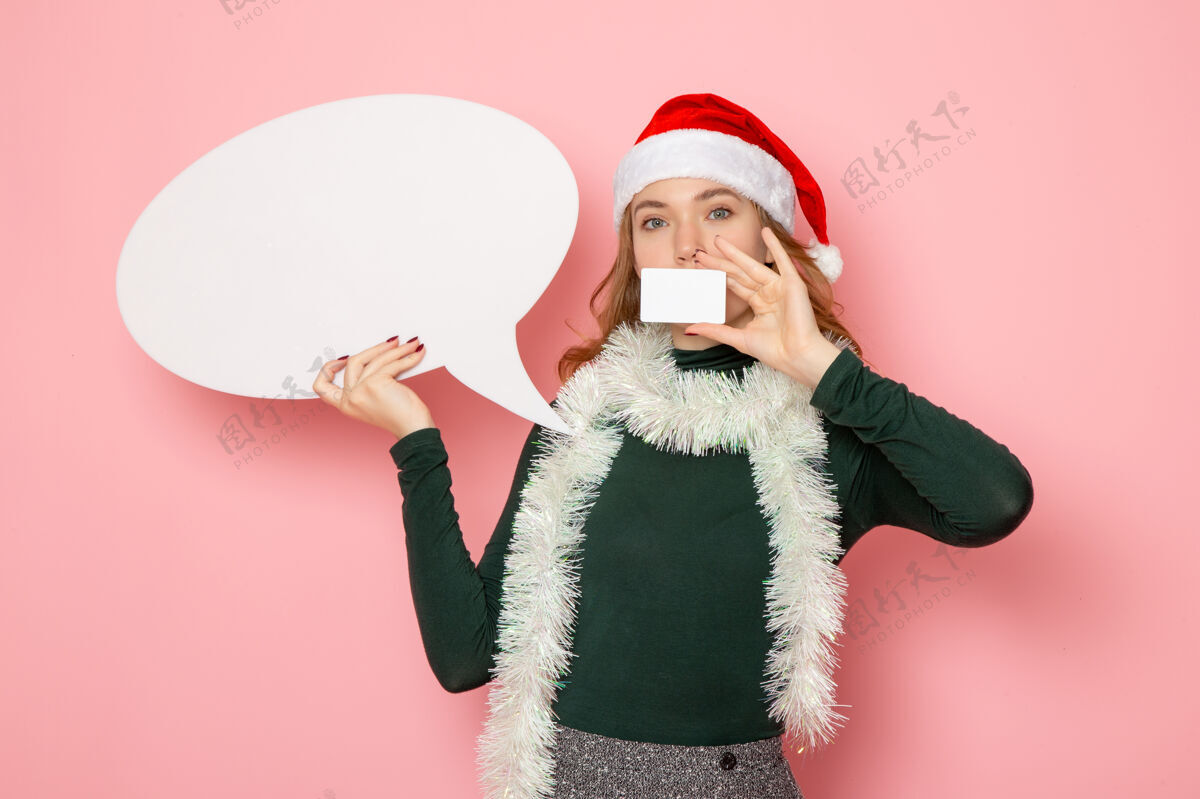 银行正面图年轻女性手持白色大招牌和银行卡在粉色墙上的模特节日圣诞新年感慨年轻女性大成人