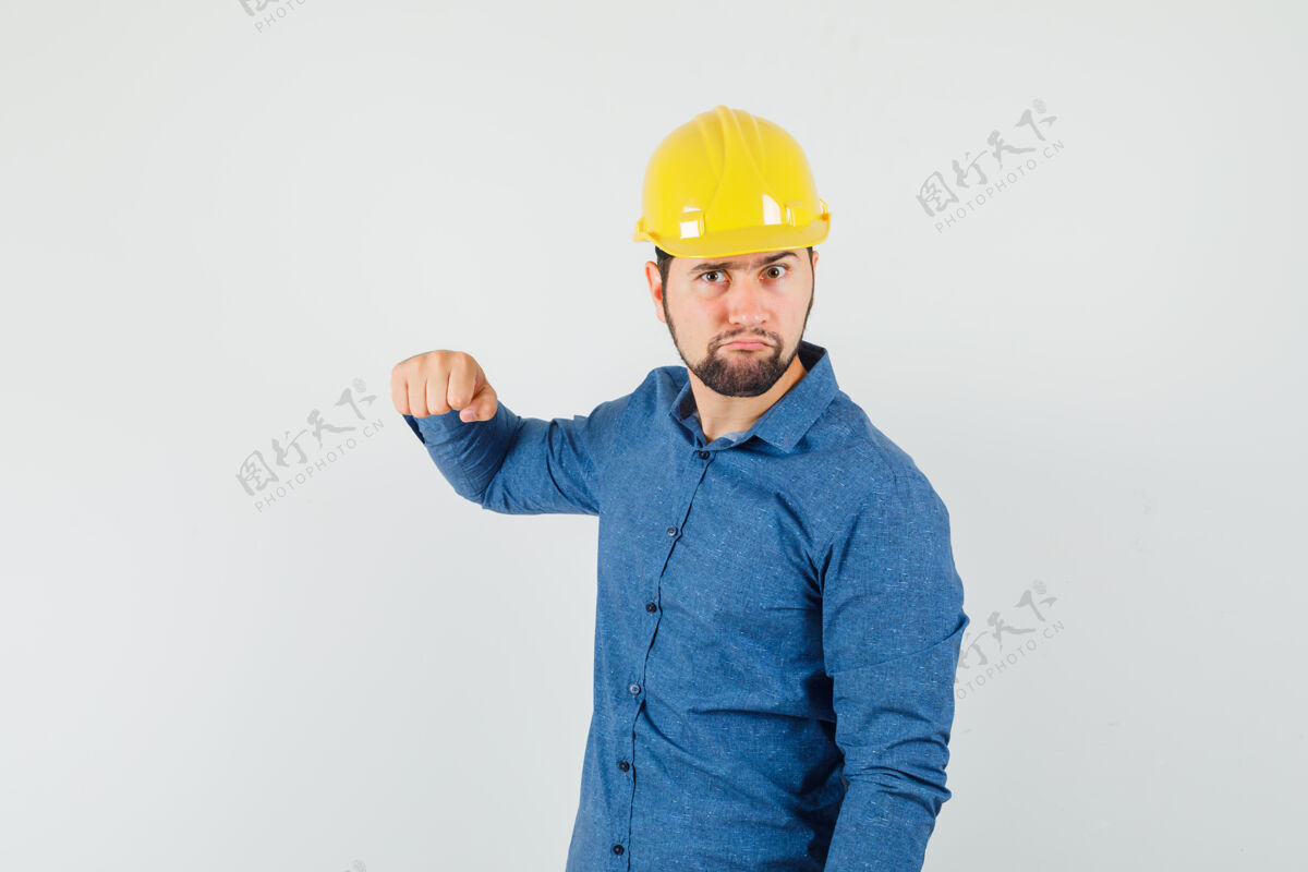 专业年轻工人用拳头威胁衬衫 头盔 看上去很紧张沟通工厂拳头