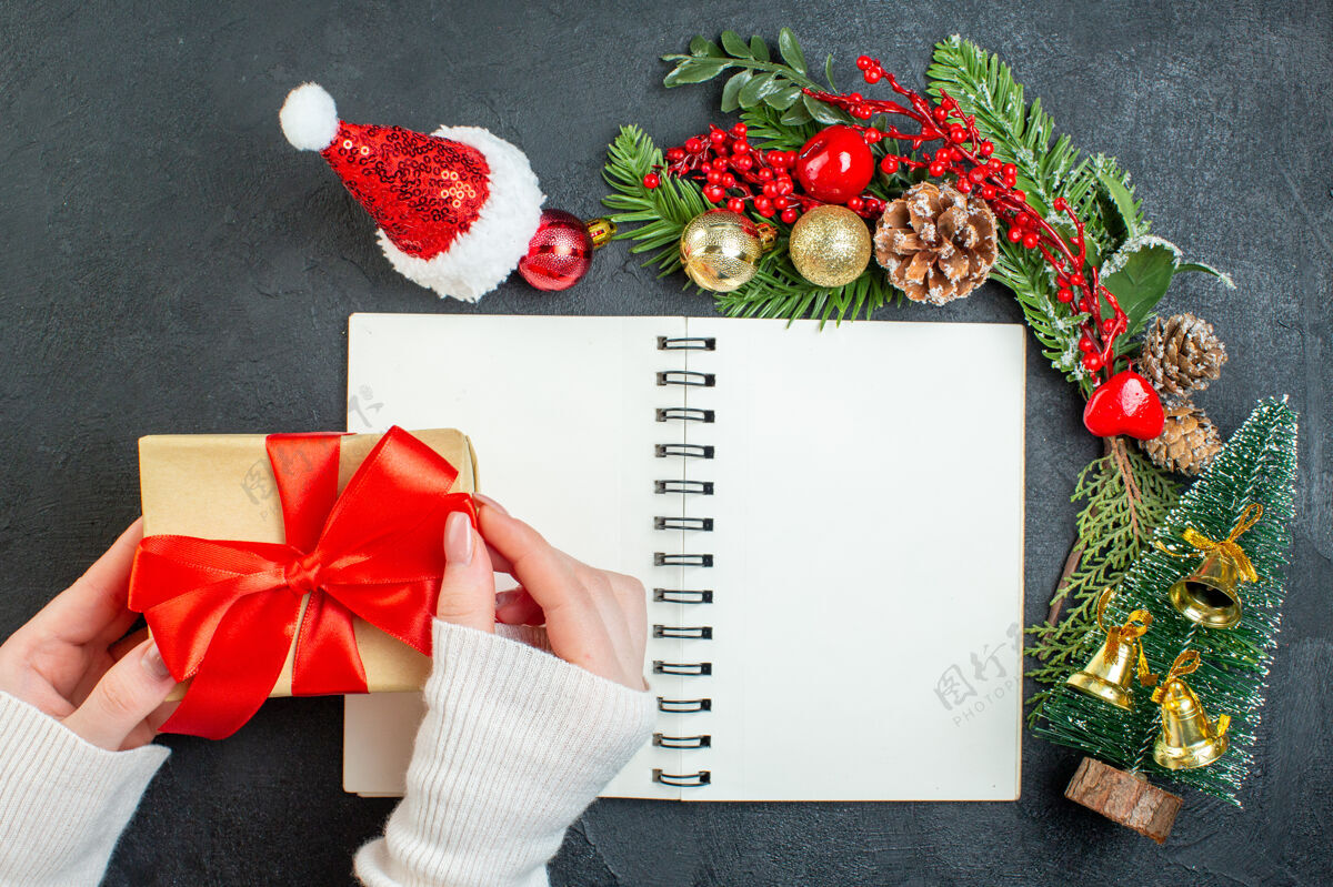 树枝顶视图圣诞气氛与杉木枝圣诞老人帽子手持礼品盒与红丝带在黑暗的背景帽子冬青树圣诞老人