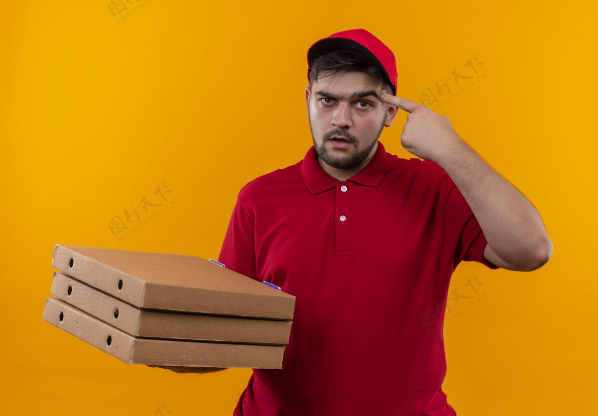 帽子年轻的送货员身穿红色制服 头戴鸭舌帽 手里拿着一叠披萨盒 指着自己的太阳穴 一脸严肃地专注于任务年轻人指着任务