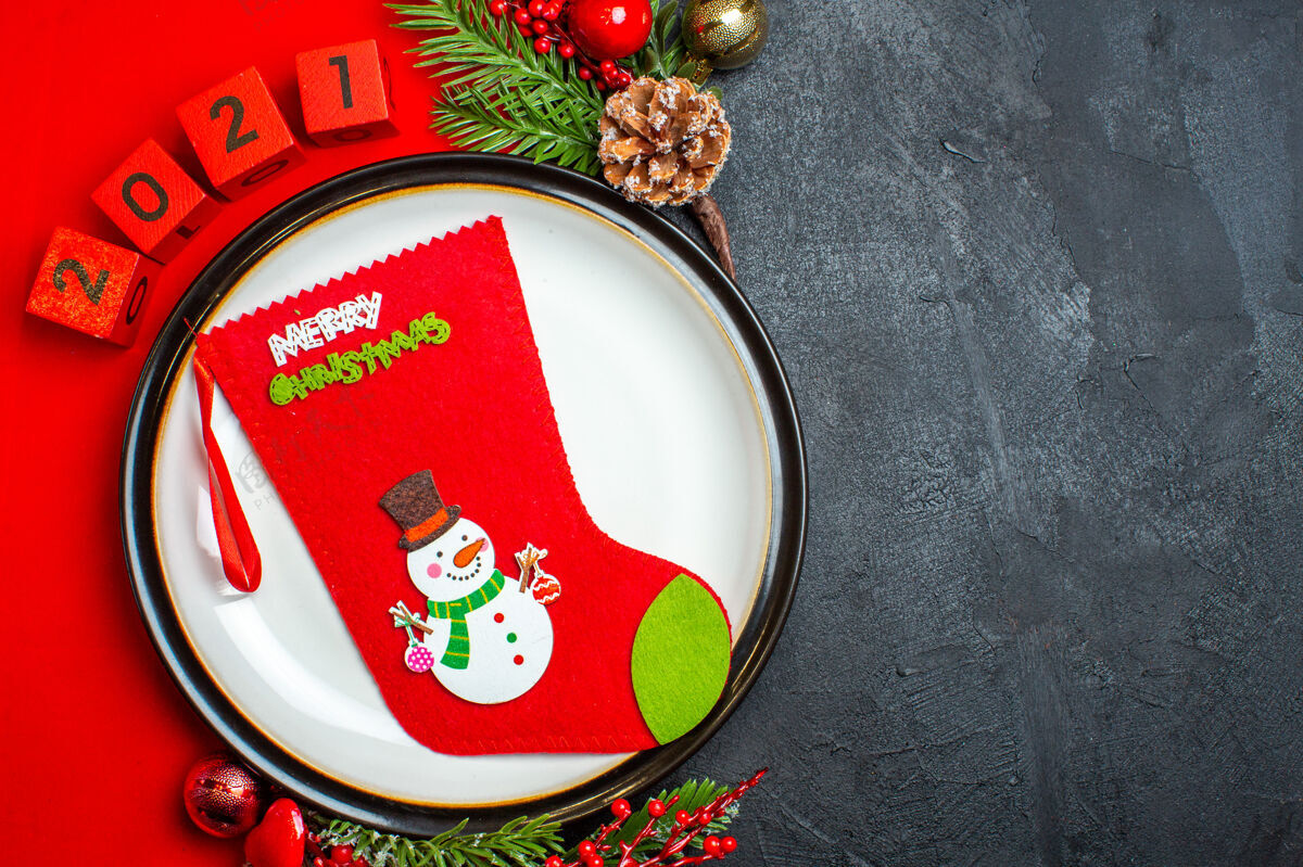 头顶新年背景俯视图 圣诞袜子放在餐盘上装饰配件杉木树枝和数字放在黑色桌子上的红色餐巾上袜子座位数字