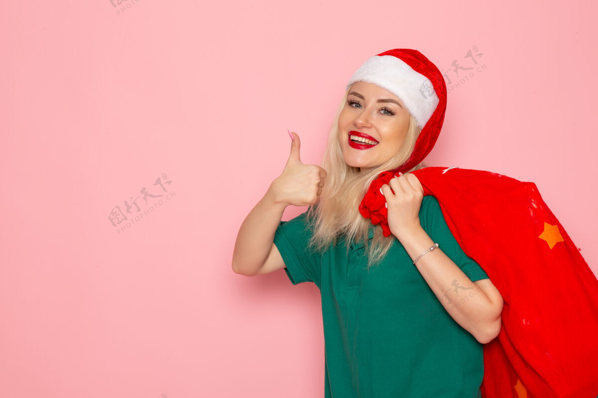携带正面图：年轻女性手拿红包 粉色墙壁上有礼物模特圣诞新年照片彩色圣诞老人假期色彩风景圣诞