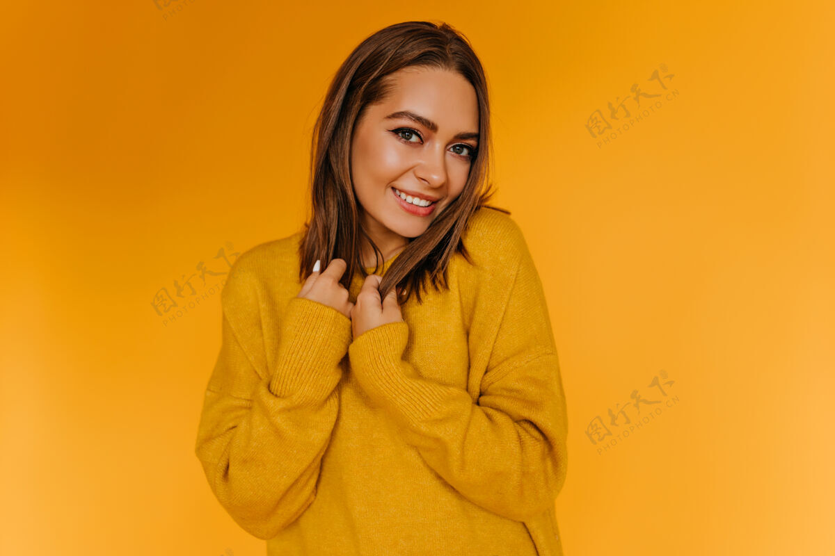 魅力害羞的欧洲女人在橙色的墙上微笑着摆姿势穿着黄色毛衣的迷人女孩玩得很开心积极快乐放松