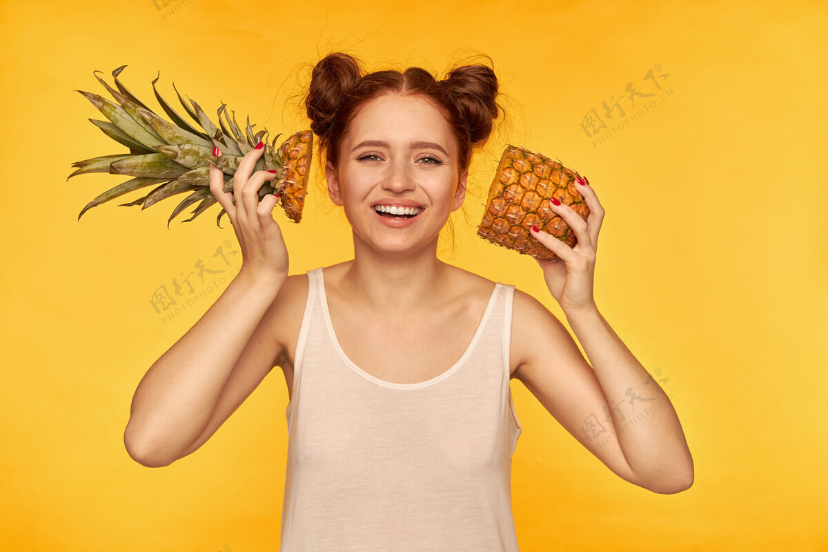 皮肤年轻的女士 漂亮的姜黄色的女人 带着两个小面包穿着白衬衫 把切好的菠萝放在脸旁 面带微笑 健康的生活方式隔着黄色的墙看着孤独看健康果汁