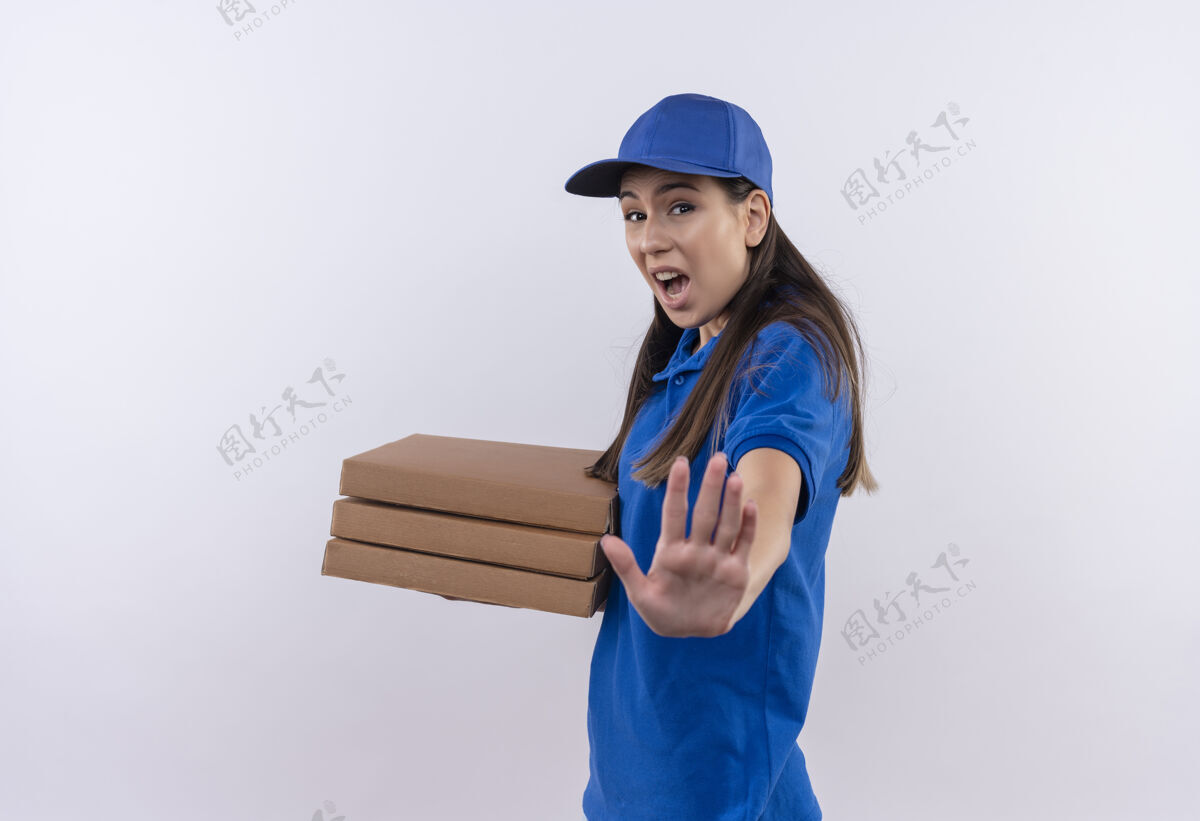 表情身穿蓝色制服 头戴鸭舌帽的年轻送货女孩手拿比萨饼盒 脸上带着恐惧的表情 在做停车标志做标志女孩