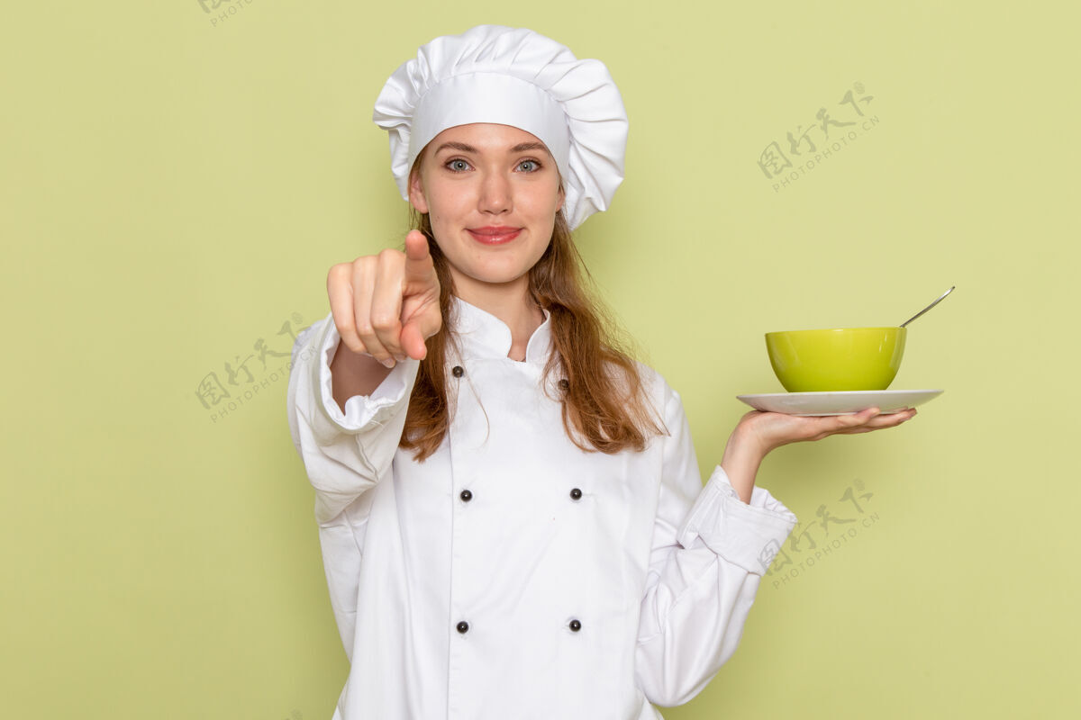 女身着白色厨师服的女厨师正拿着绿色盘子 微笑着站在绿色墙上人烹饪微笑
