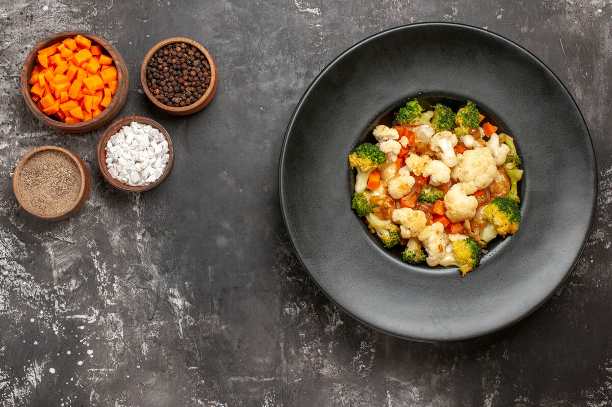 炒锅顶视图西兰花和花椰菜沙拉在黑碗不同的香料和削减胡萝卜碗在黑暗的表面复制空间香料厨房用具炊具