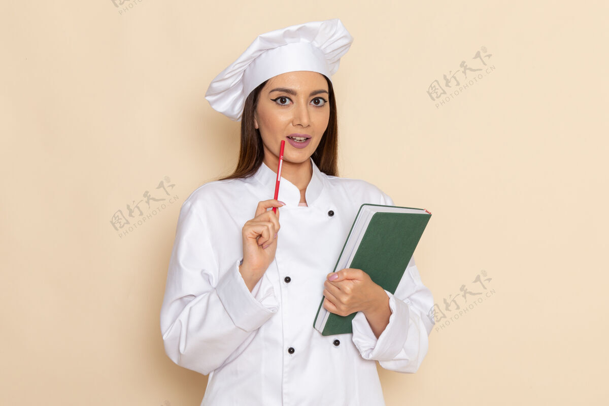 女身穿白色厨师服的年轻女厨师正对着白色墙壁 手里拿着抄写本和钢笔烹饪医疗食品