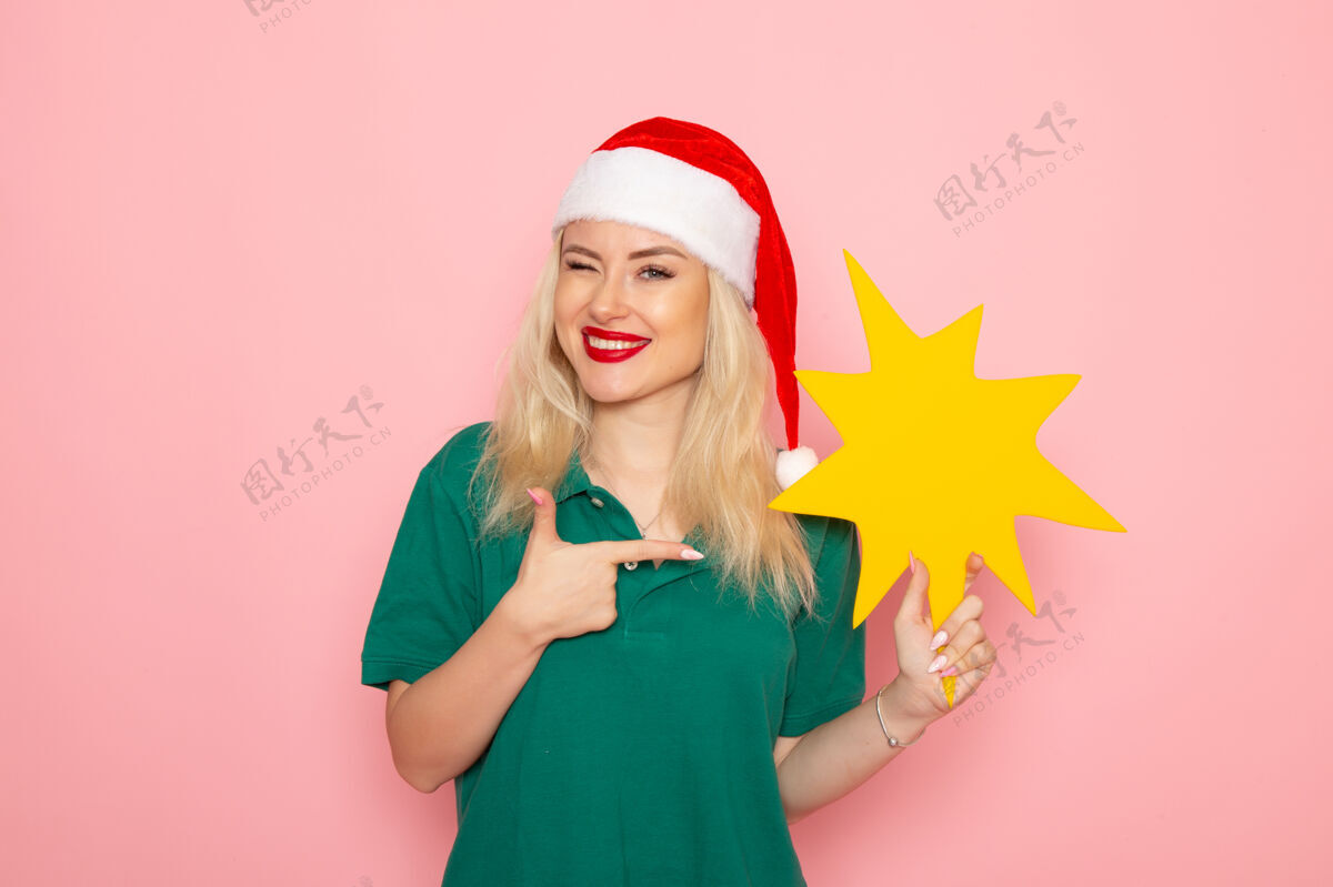 风景正面图年轻女性手持黄色大人物在粉色墙上拍照工作新年假期工作快递制服圣诞节漂亮信使