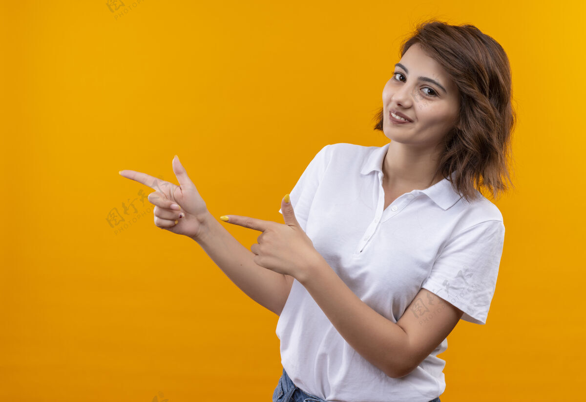 壁板短发女孩身穿白色马球衫 微笑自信地用食指指着身边橙色手指微笑
