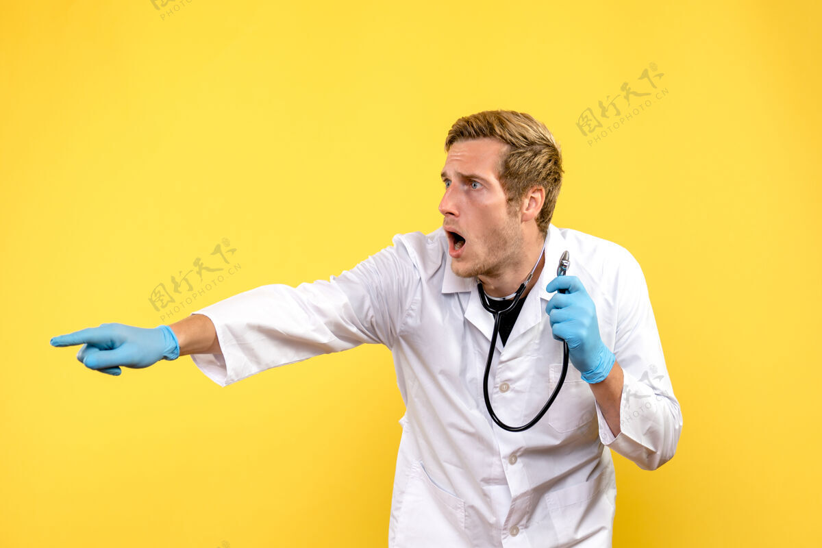 肖像正面图男医生指着黄色背景上的东西健康病毒医情专业医疗前面