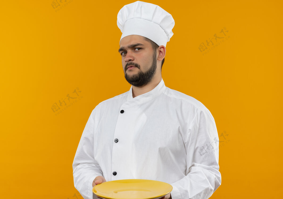 年轻穿着厨师制服 拿着空盘子的年轻男厨师被隔离在橙色的空间里制服厨师橙色