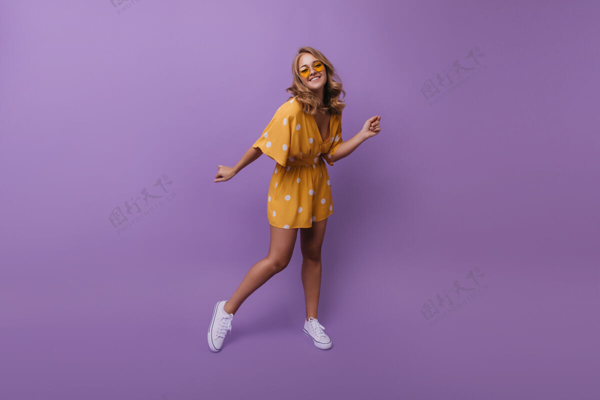 休闲穿着白色运动鞋的快乐晒黑女孩的全长肖像在紫色的肖像拍摄中快乐的金发女人跳舞的肖像瘦身年轻金发