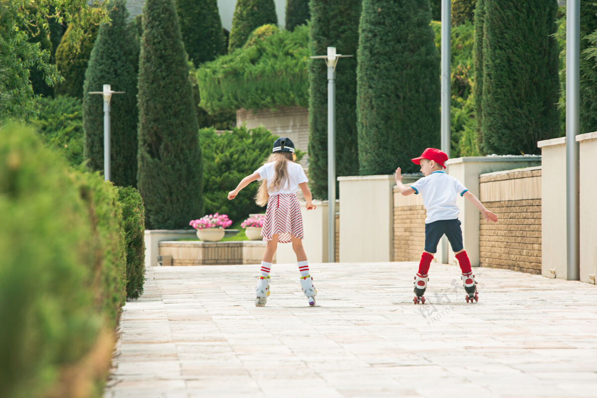 户外在公园里 一对迷人的年轻夫妇穿着溜冰鞋一起滑冰年轻的白人男孩和女孩乐趣运动装人