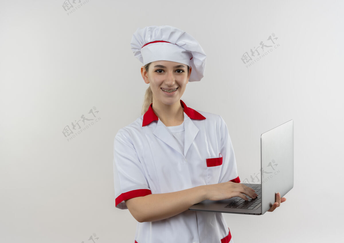 微笑面带微笑的年轻漂亮厨师身着厨师制服 戴着牙套 拿着笔记本电脑 在空白处显得很孤立制服笔记本电脑漂亮