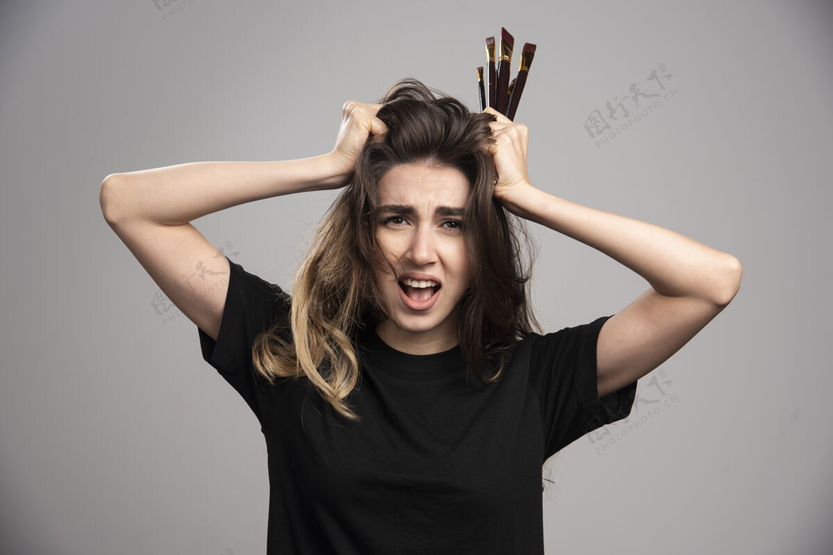 情感愤怒的女人拿着刷子在灰色的墙上摸她的头发年轻休闲女孩