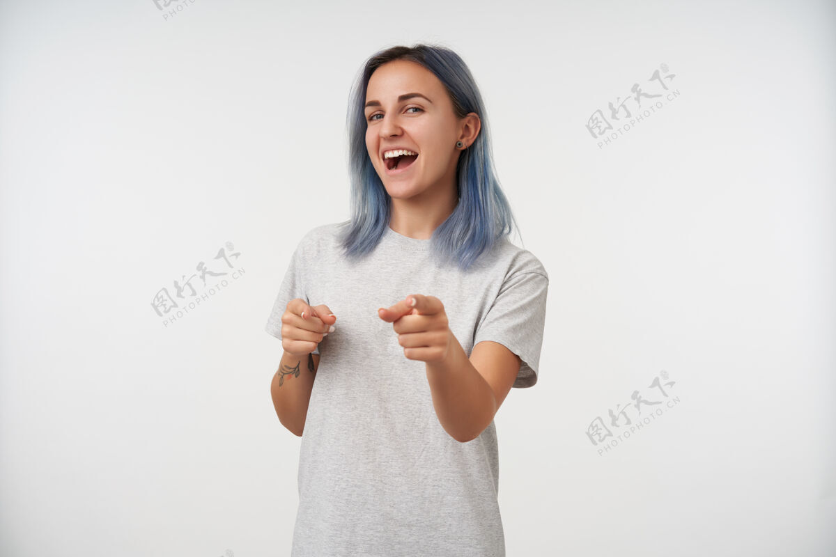 化妆品年轻快乐的纹身女士的肖像 蓝色短发举起双手 用食指快乐地展示 孤立于白色显示自然基本