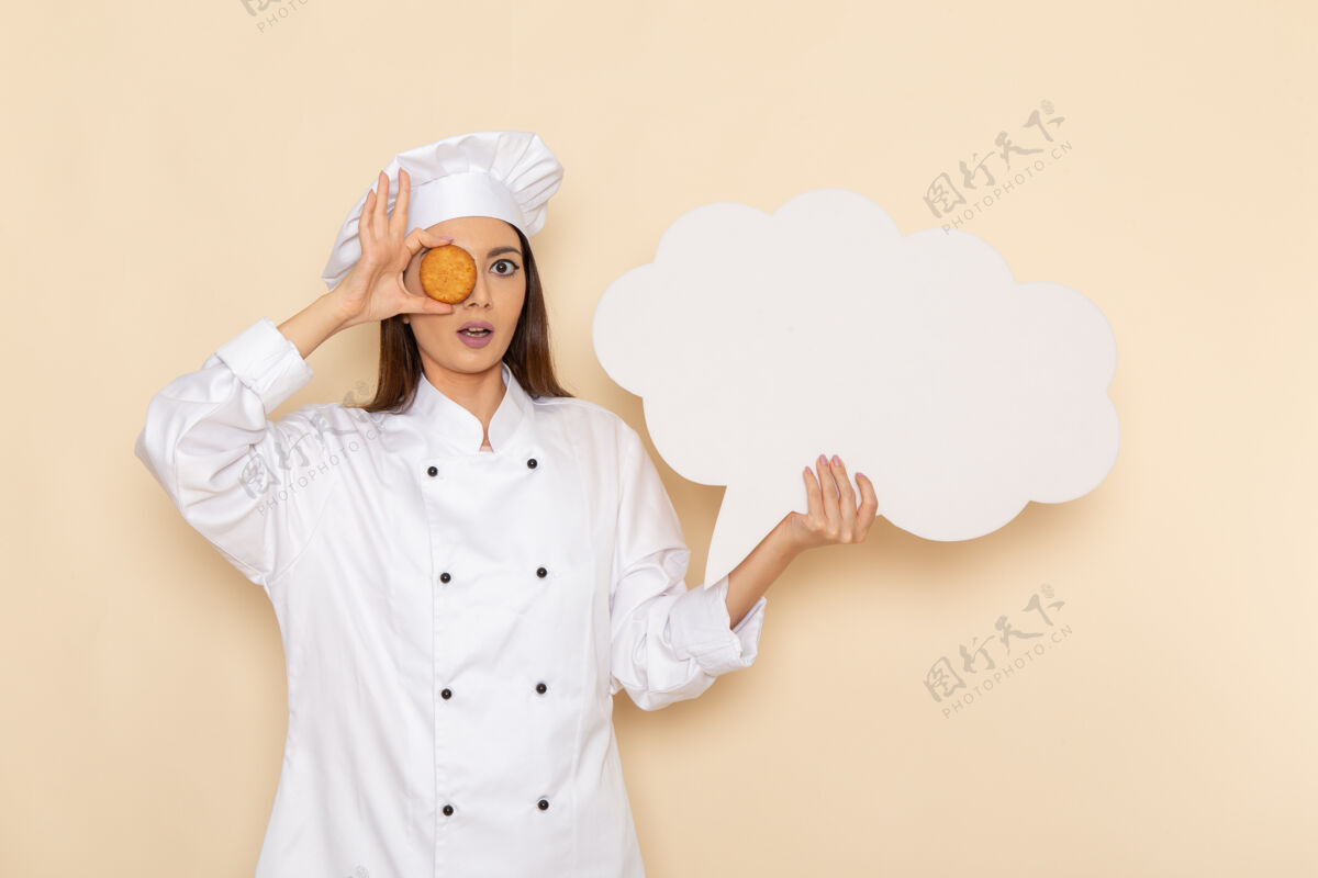 前面身穿白色厨师服的年轻女厨师的正面图 白色墙上拿着白色的牌子和饼干专业人肖像