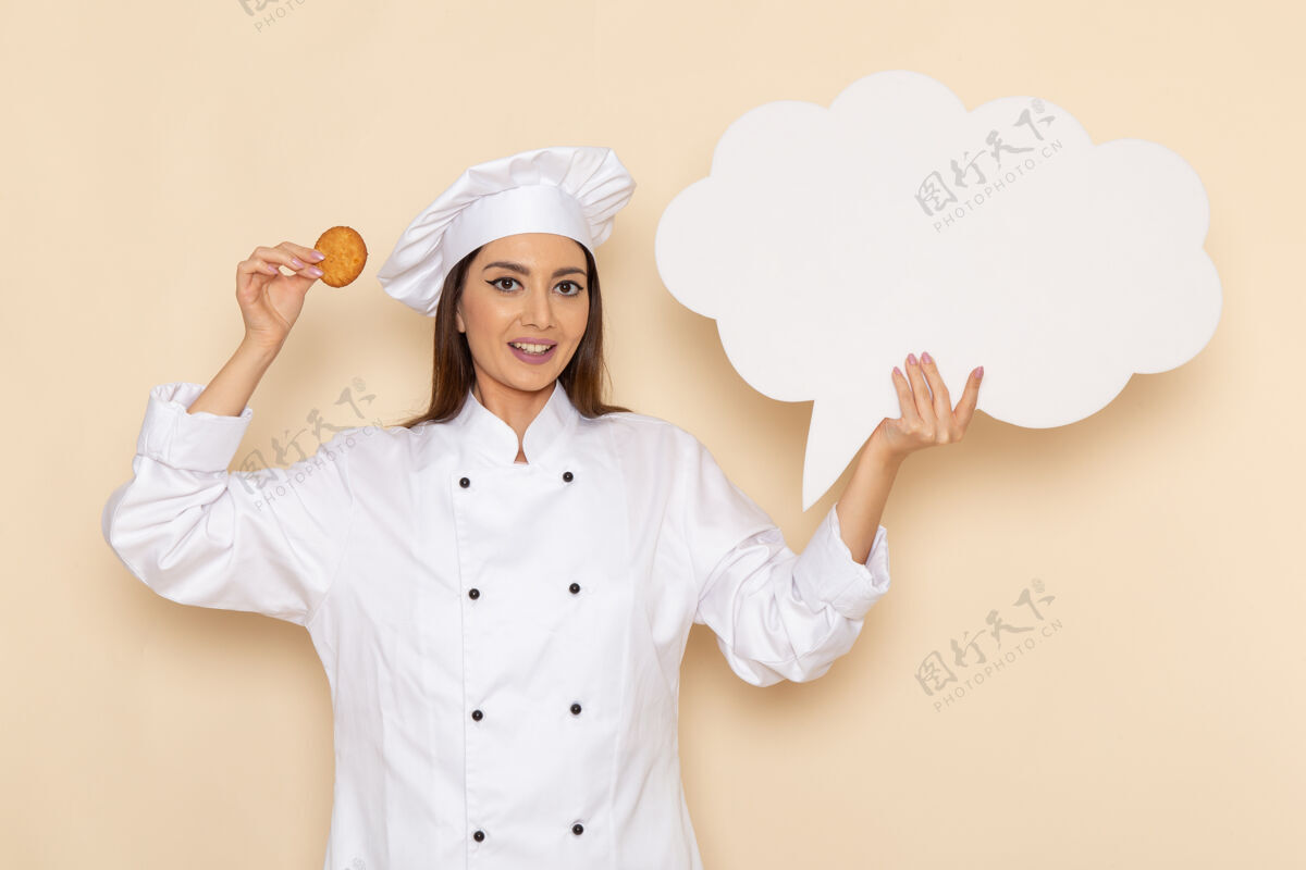 厨房身穿白色厨师服的年轻女厨师的正面图 白色墙上拿着白色的牌子和饼干人西装前面