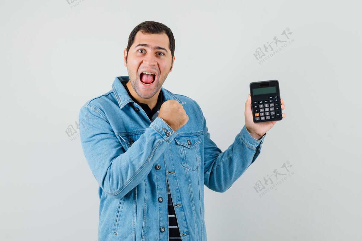 手势身穿t恤衫 夹克衫的年轻人手持计算器 摆出胜利者的姿态 看上去很开心计算器衬衫商人
