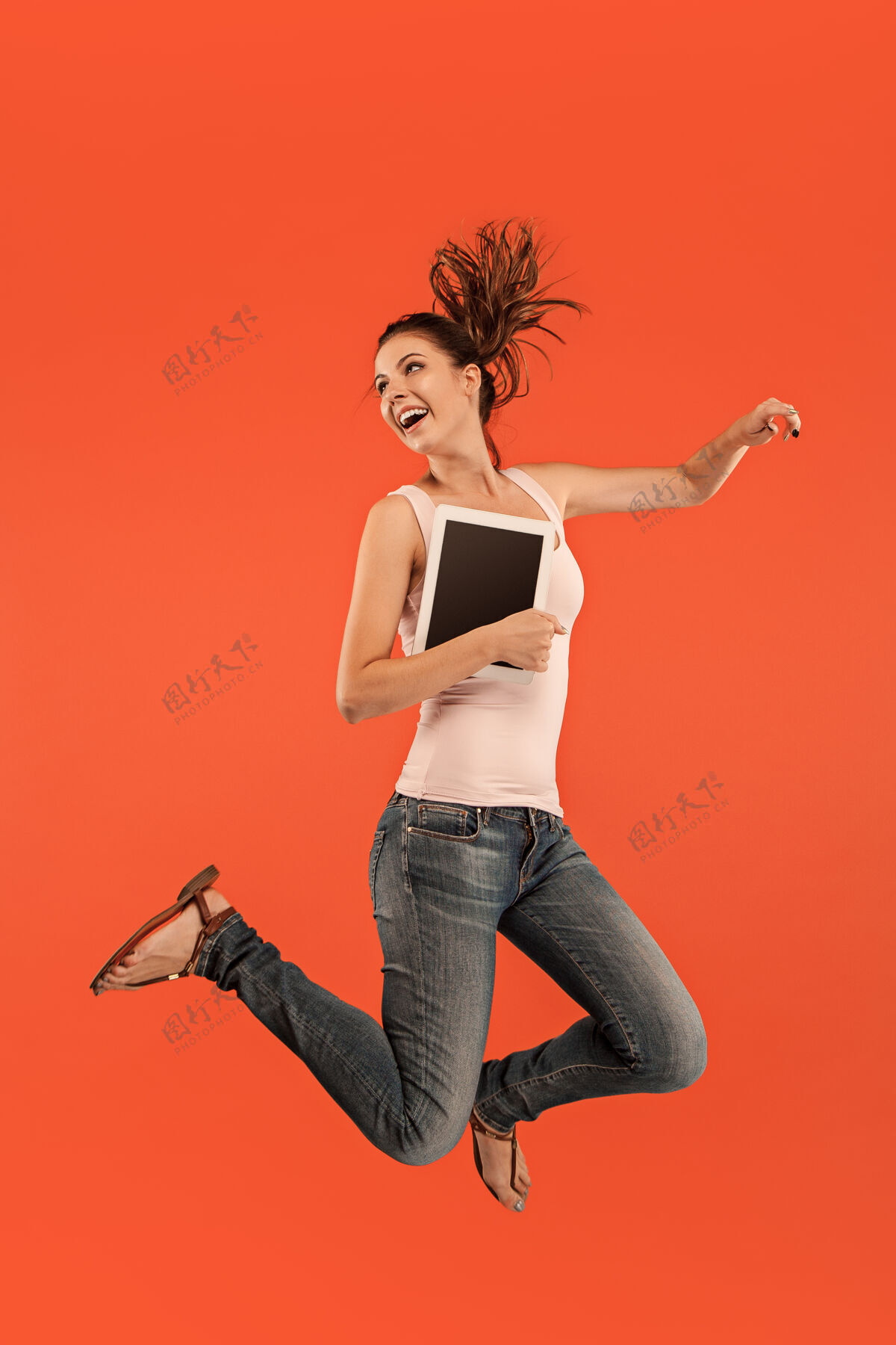 成人年轻女子跳跃时使用笔记本电脑或平板电脑小玩意越过蓝色奔跑的女孩在运动或运动工作绿色休闲