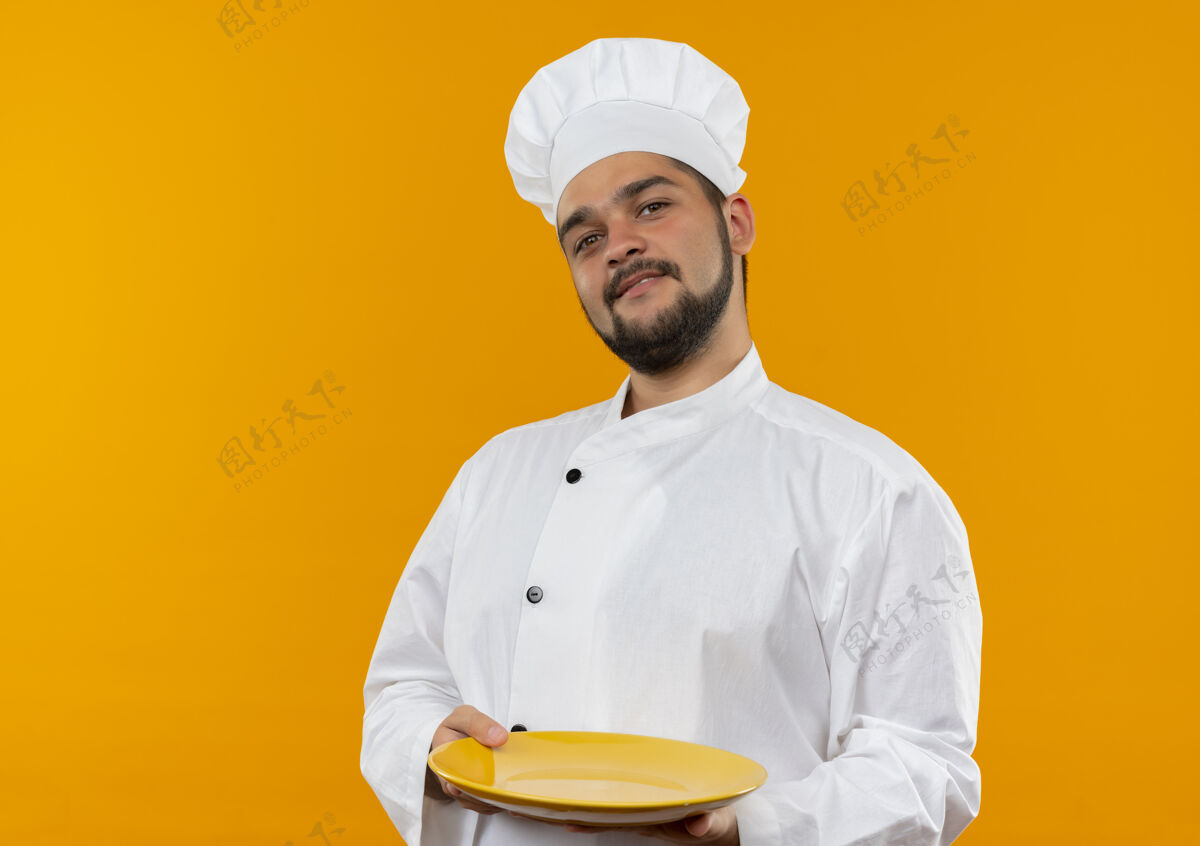 厨师身着厨师制服的年轻男厨师手拿着空盘子 看上去孤立在橙色的空间里橙色盘子制服