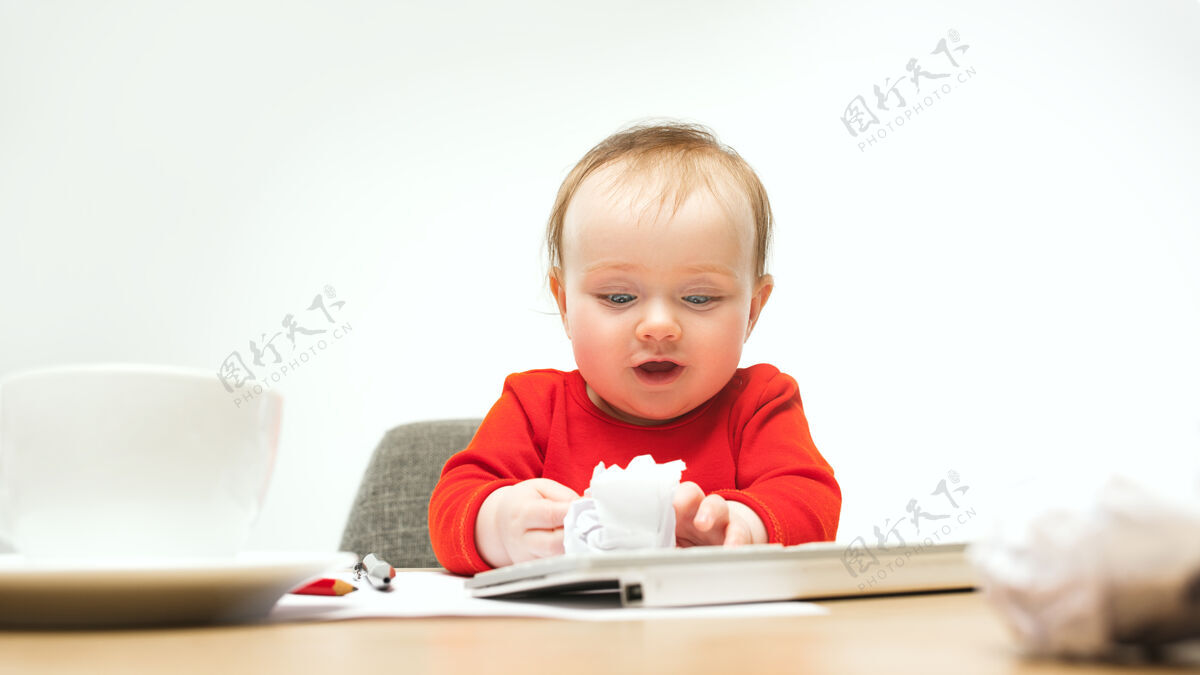 童年快乐的小女婴坐在一个白色的工作室里 用现代电脑或笔记本电脑的键盘科技年轻房子