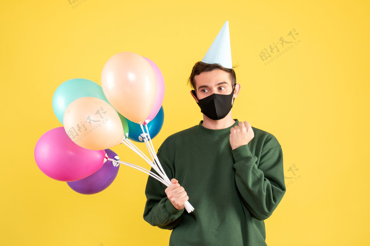 帽子正面图体贴的年轻人戴着派对帽 站在黄色的气球上生日乐趣喜剧演员