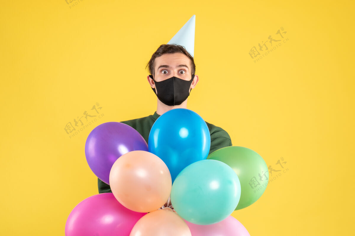 生日正面图：戴着派对帽 站在黄色地面上的五颜六色气球的大眼睛年轻人气球男人乐趣