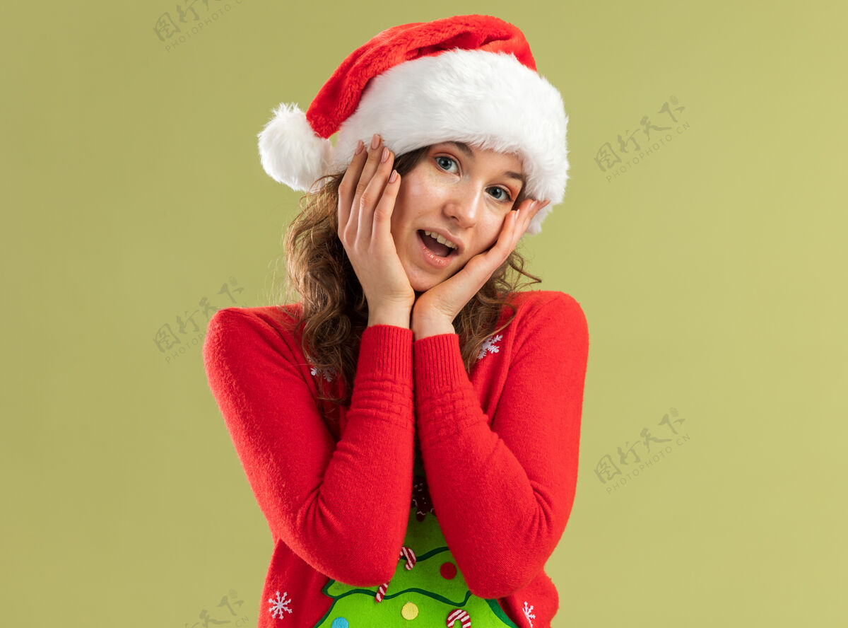 微笑穿着红色圣诞毛衣 戴着圣诞帽的年轻女子 脸上洋溢着幸福和积极的笑容绿色看新
