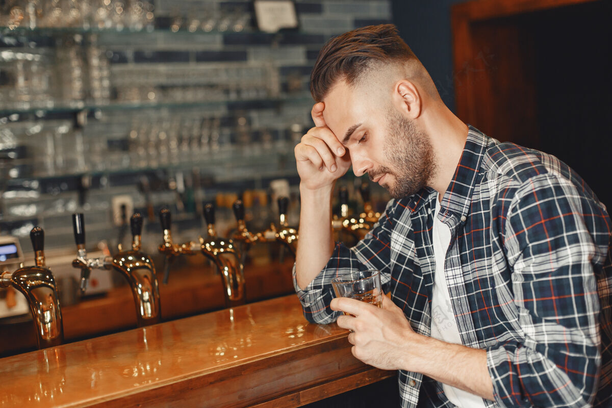饮料一个穿衬衫的男人手里拿着一个玻璃杯那个家伙正坐在酒吧里 抱着他的头顾客男性啤酒厂
